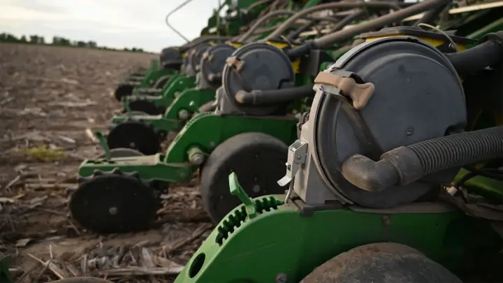 A row of green planters sits in a field, ready for planting. These machines are essential for farmers, contributing to the average hours on a tractor per year.